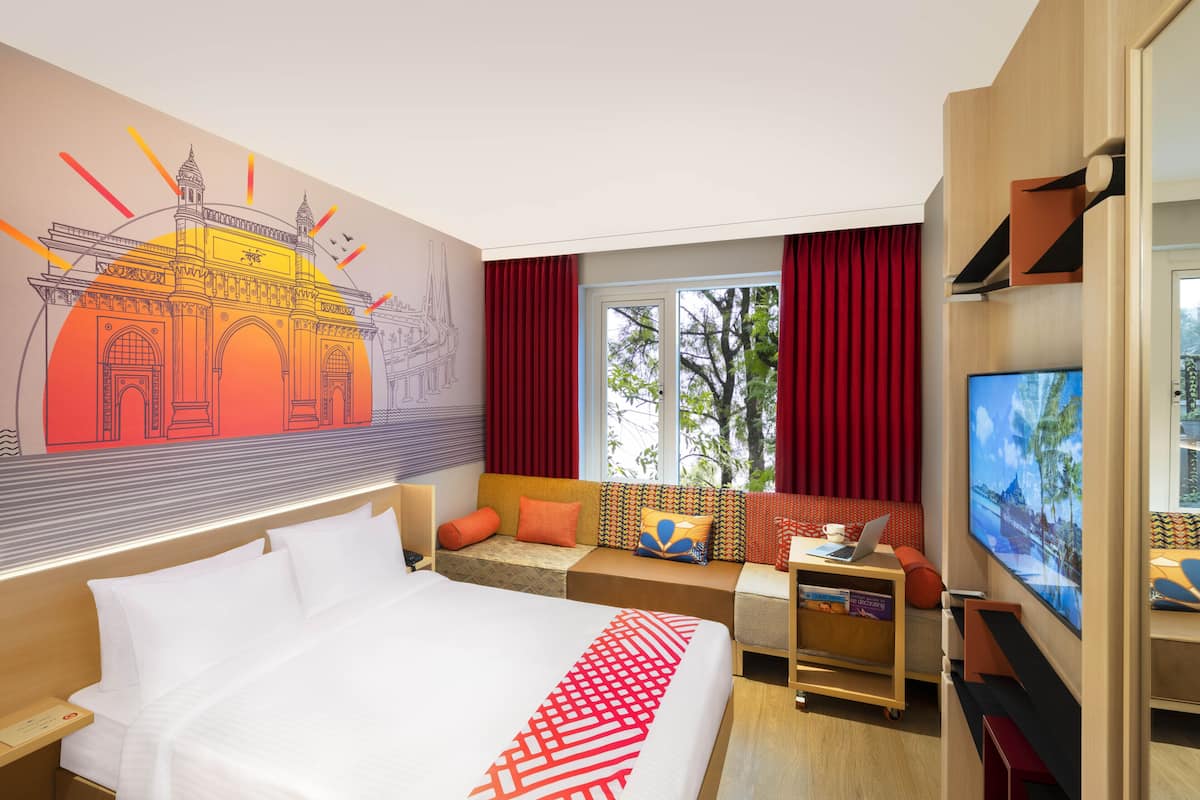 Ett hotellrum med en stor säng, en sittgrupp med utsikt över träd, en tv och en väggmålning.