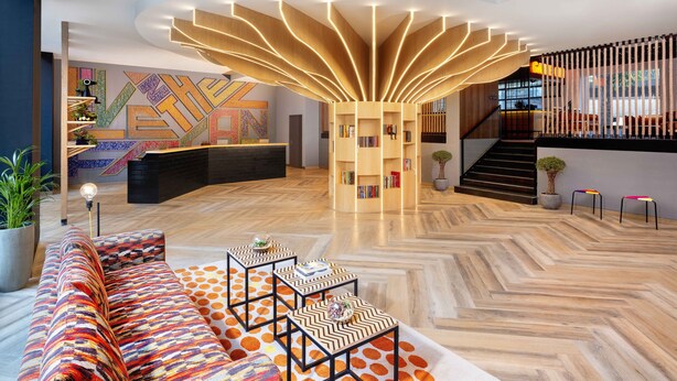 Eine moderne Lobby mit einer zentralen Treppe, einer Rezeption und einem gemusterten Sofa.