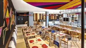 Ein modernes Restaurant mit einem langen Gemeinschaftstisch, einzelnen Tischen und einem farbenfrohen Decken-Design.