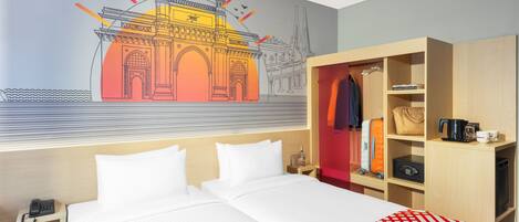 Quarto de hotel com cama, mesa de cabeceira com telefone, guarda-roupa e um mural na parede.