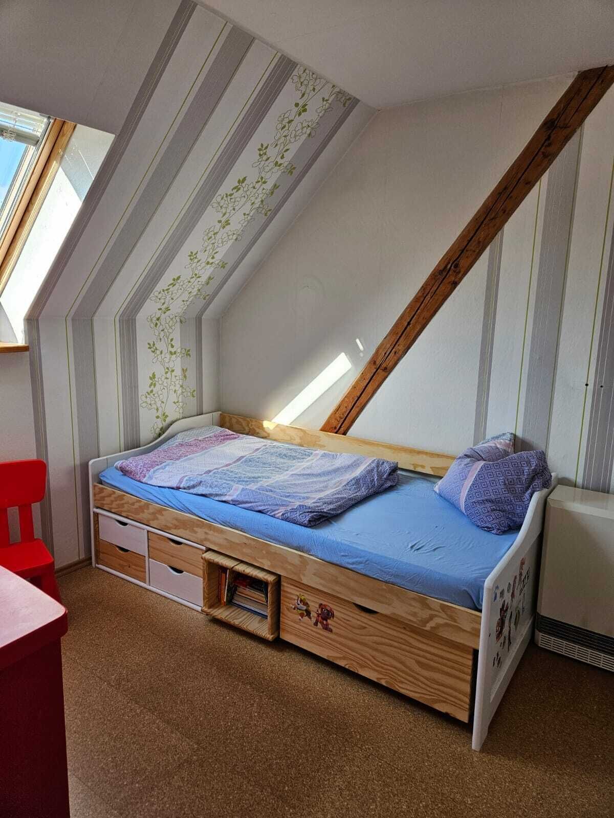 Un dormitorio pequeño con techo inclinado, una cama individual, una silla roja y una mesita.