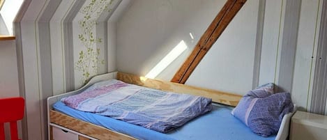 Un dormitorio pequeño con techo inclinado, una cama individual, una silla roja y una mesita.