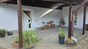 Eine überdachte Terrasse mit Backsteinboden, Holzstühlen und Topfpflanzen.