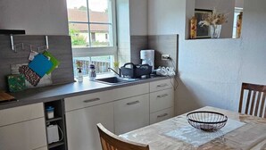 Eine moderne Küche mit Holzboden, einem Esstisch mit Stühlen und einem Fenster mit Blick auf einen Garten.