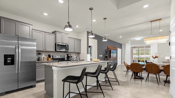 A modern kitchen with stainless steel appliances, a central island with bar stools, pendant lighting, and a view to the dining area. - Poolside Oasis · Family Home Close to Disney (Davenport)