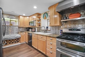 Una cocina compacta con armarios de madera, microondas integrado, estufa de acero inoxidable y un botellero.