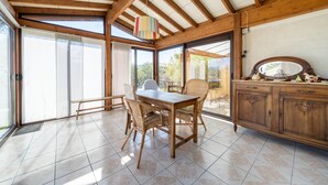 A dining area with a wooden table and chairs, a cabinet with decorative items, and large windows allowing natural light. - House in Drôme Provençale (Dieulefit)