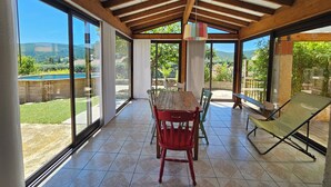 A covered patio with a wooden ceiling, large glass doors, a wooden table with chairs, and a green lounge chair. - House in Drôme Provençale (Dieulefit)