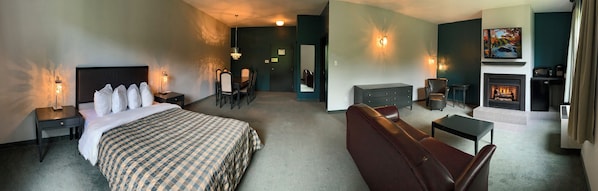 A hotel room with a large bed, a leather sofa, a dining table with chairs, a fireplace, and a view of the dining area. - Auberge Val Saint-Côme (Saint Come)