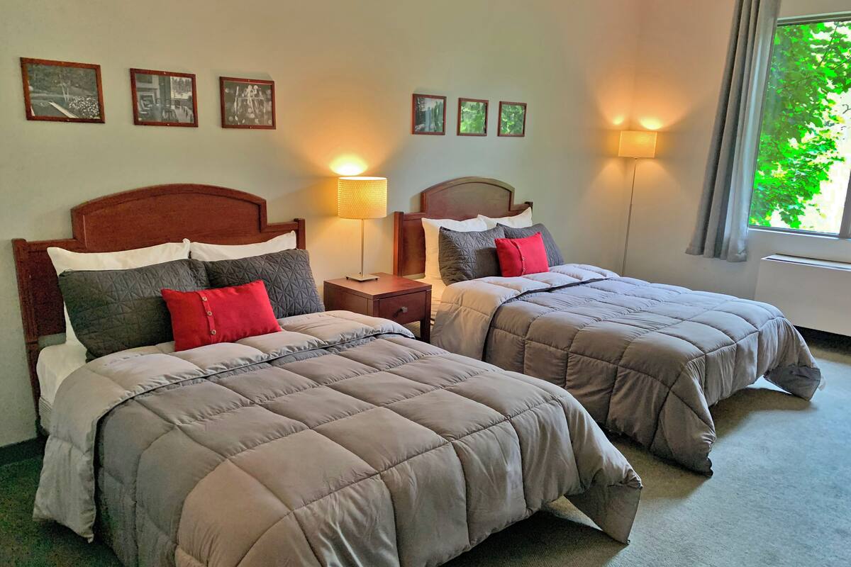 A hotel room with two beds, each with a wooden headboard, a nightstand, a lamp, and framed pictures on the wall.