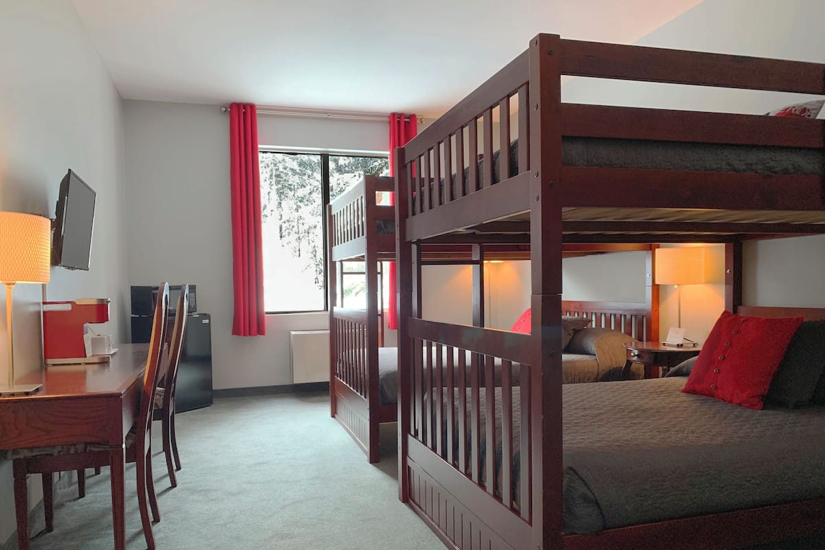 A bunk bed room with a desk, chair, and a TV.