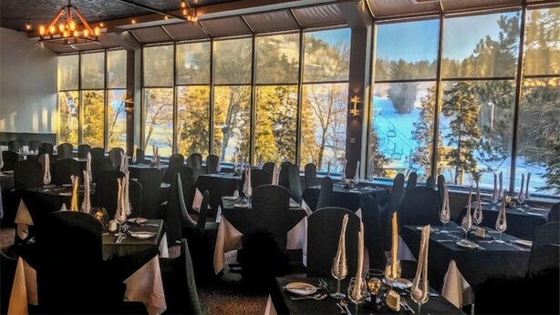 A restaurant with tables set for dining, large windows with a view of a snowy landscape. - Auberge Val Saint-Côme (Saint Come)