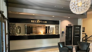 A reception area with a sign labeled "RECEPTION," a phone, a cabinet with glassware, and a patterned carpet. - Auberge Val Saint-Côme (Saint Come)