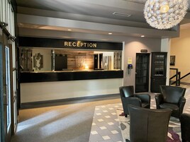 Un área de recepción con un cartel que dice "RECEPTION", un teléfono, un mueble con cristalería y una alfombra estampada.