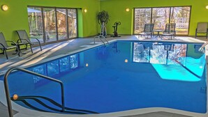 An indoor swimming pool with clear glass walls, multiple lounge chairs, and a bright green wall. - Auberge Val Saint-Côme (Saint Come)