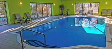 Una piscina interior con paredes de vidrio transparente, múltiples sillones de descanso y una pared de color verde brillante.