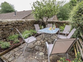 An outdoor patio with a stone wall, a table with chairs, and a small tree.