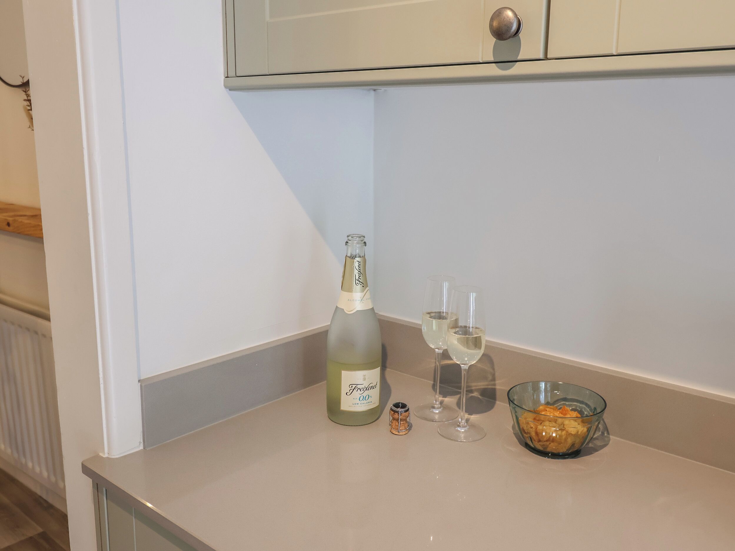 Una botella de champán Freixenet, dos copas y un bol de aperitivos sobre una encimera de cocina.