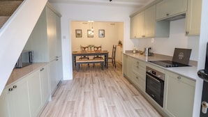 Eine moderne Küche mit hellem Holzboden, einem Essbereich mit Holztisch und Stühlen sowie hellgrünen Schränken.