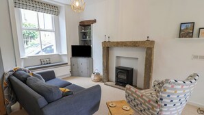 Ein Wohnzimmer mit einer Couch, einem gemusterten Sessel, einem kleinen Holztisch, einem Kamin, einem Fernseher und einem dekorativen Regal.