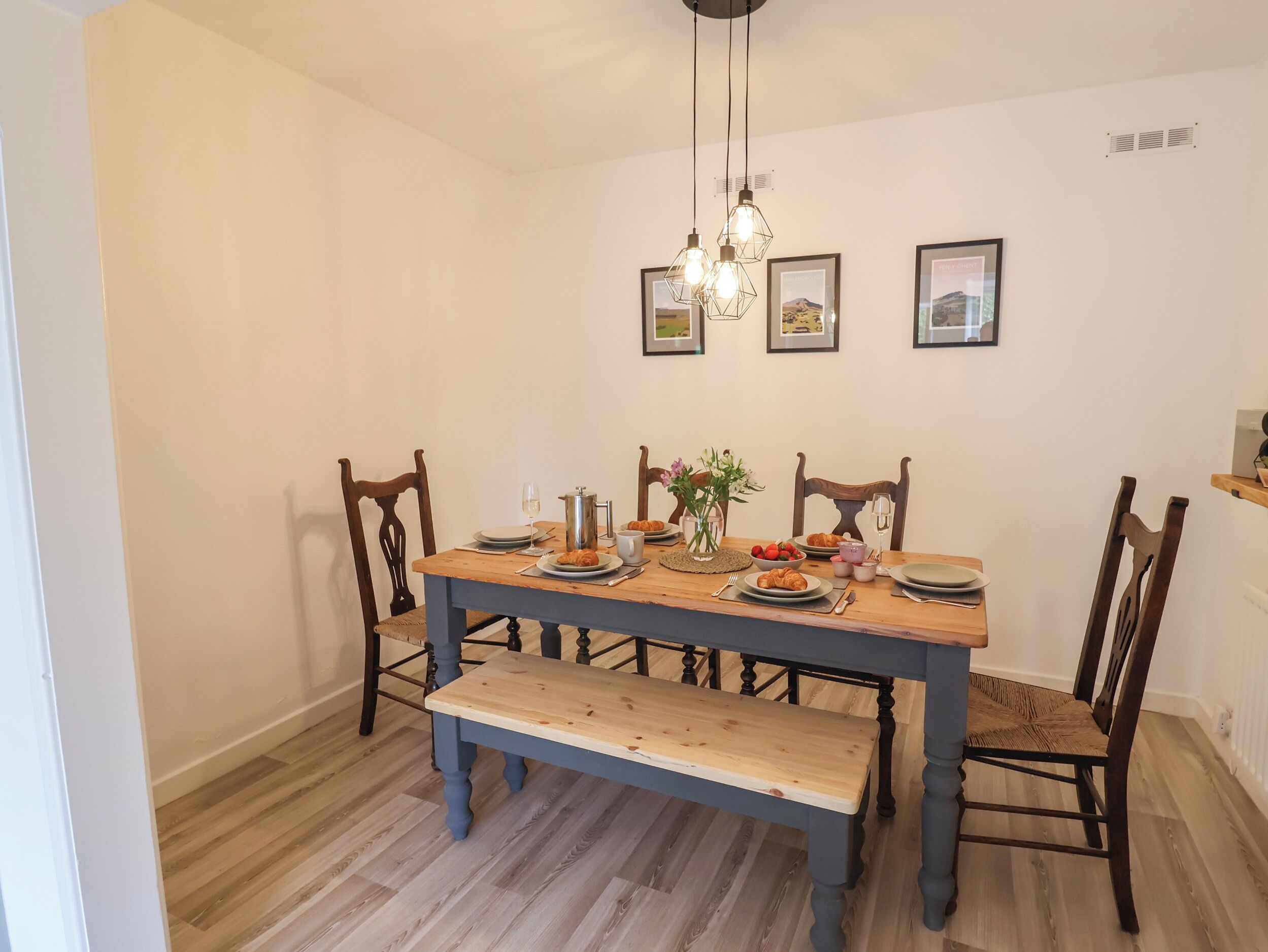 A dining room with a wooden table, chairs, a bench, and a chandelier.
