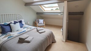 Ein Schlafzimmer mit Oberlicht, einem Bett mit gemustertem Überwurf, einem Sessel und einem Nachttisch mit Lampe.