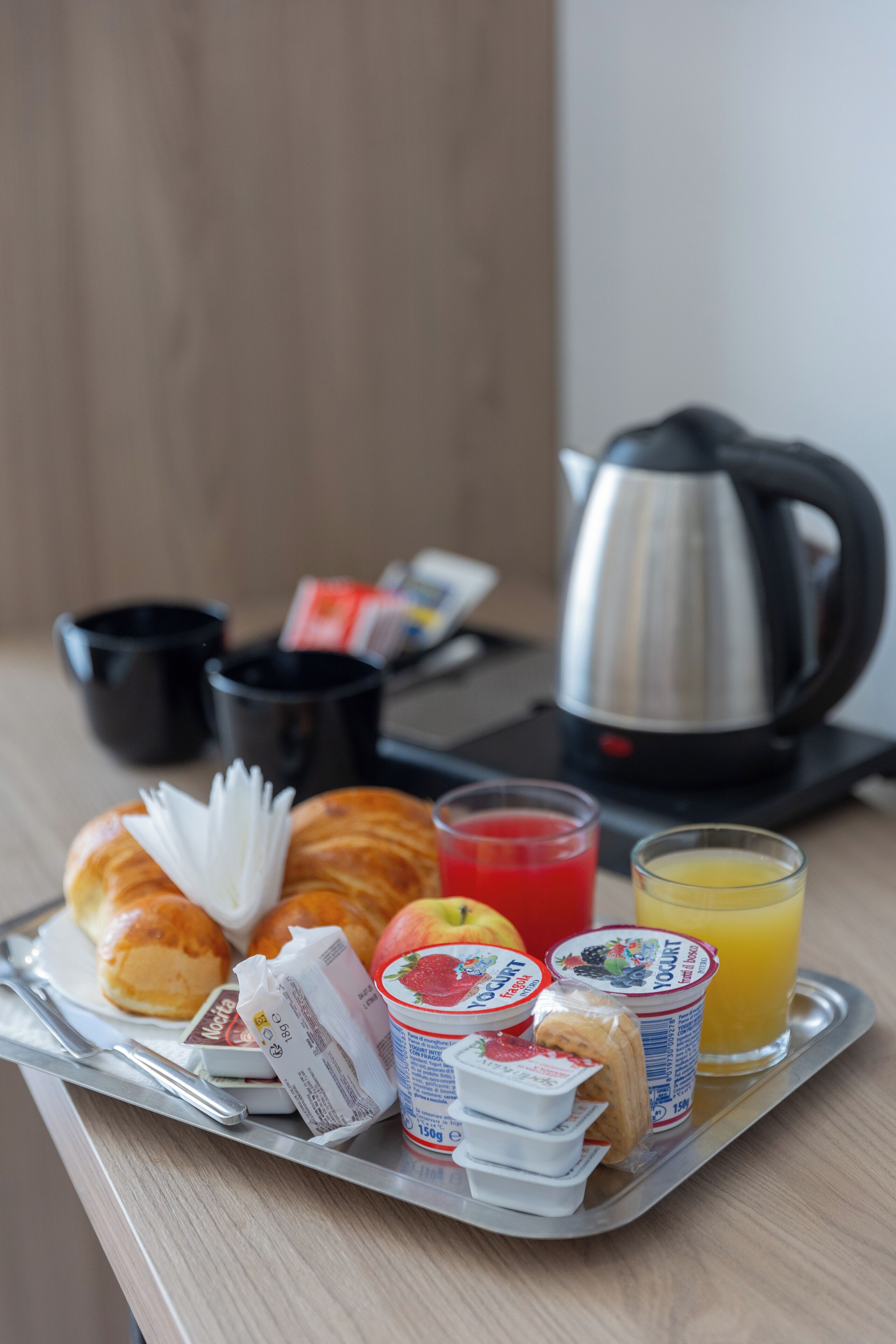 A tray with breakfast items including croissants, yogurt, a banana, and juice.