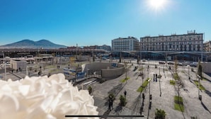 An airport terminal with a large central building, a parking area, and a mountainous backdrop. - Napoli Forever (Naples)