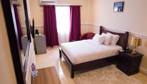 Relax in comfort with a neatly made bed, a desk for work, and a chair by the window.