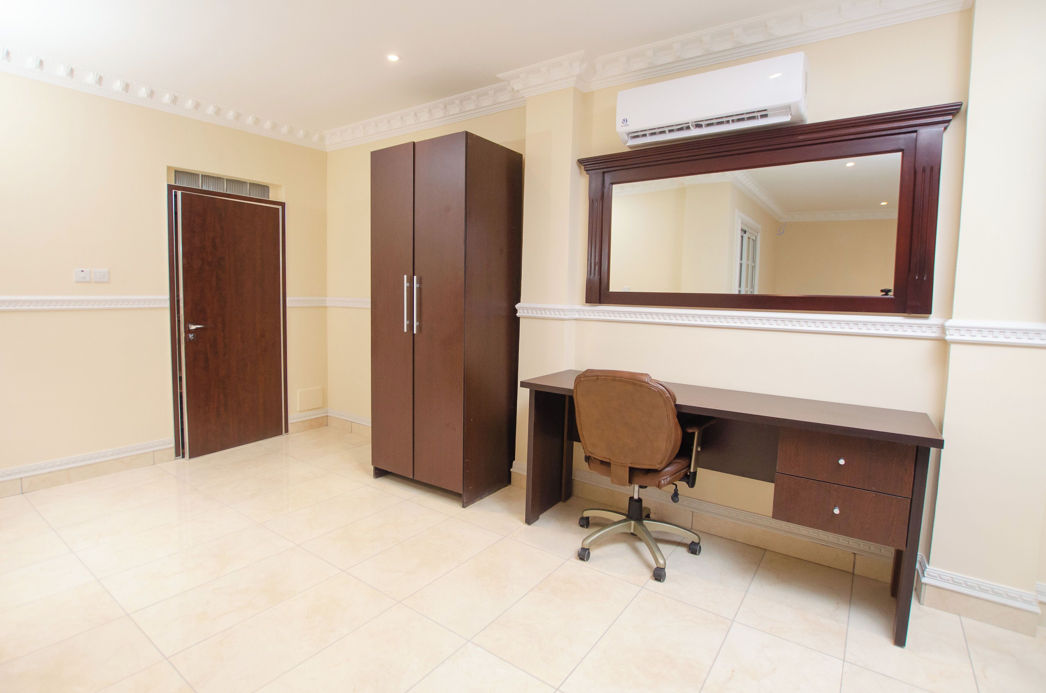 Une pièce comprenant un bureau, une chaise, une armoire et un grand miroir.