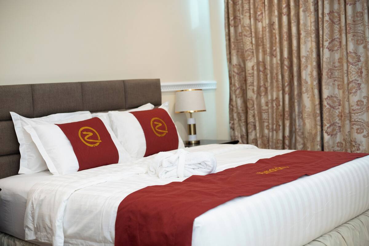 A neatly made bed with white and red bedding, a grey headboard, and a red throw blanket.