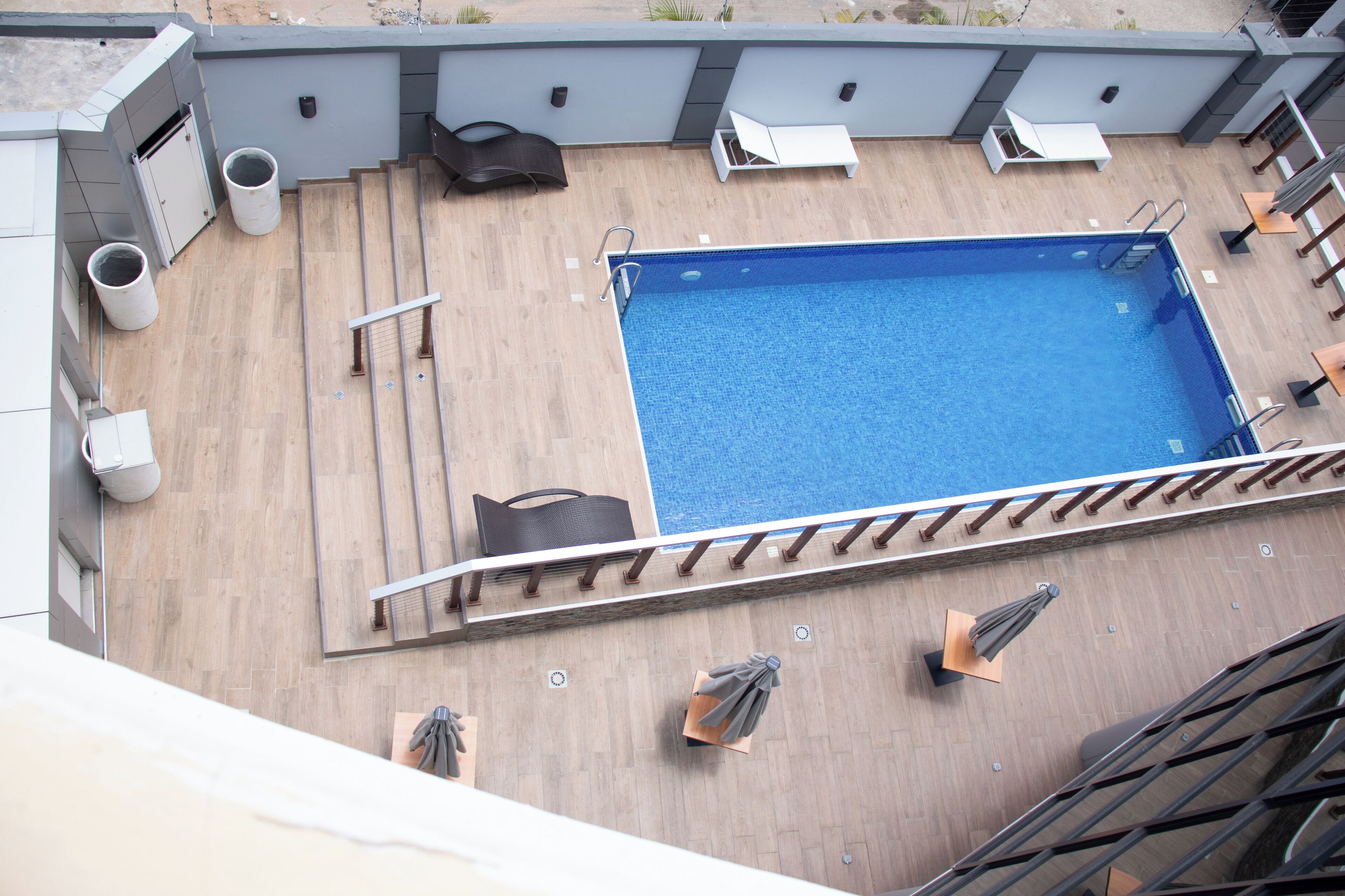 A rooftop pool area with a blue pool, lounge chairs, and umbrellas.