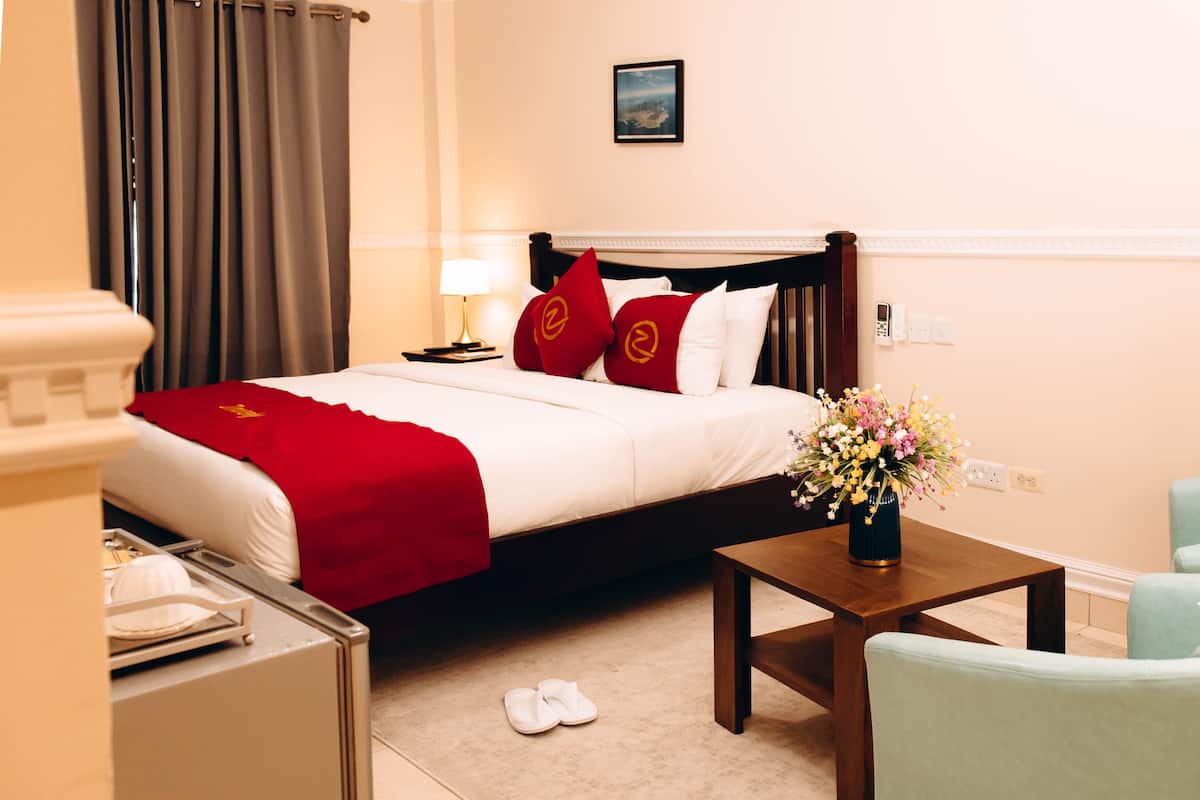 A hotel room with a bed, a nightstand, a table with a vase of flowers, a chair, and a view of the outdoors.
