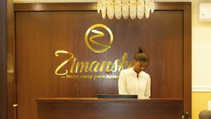 A reception desk with a chandelier, a ceiling fan, and a sign that reads "Zimansky...home away from home." - Zimansky Hotel  (Accra)