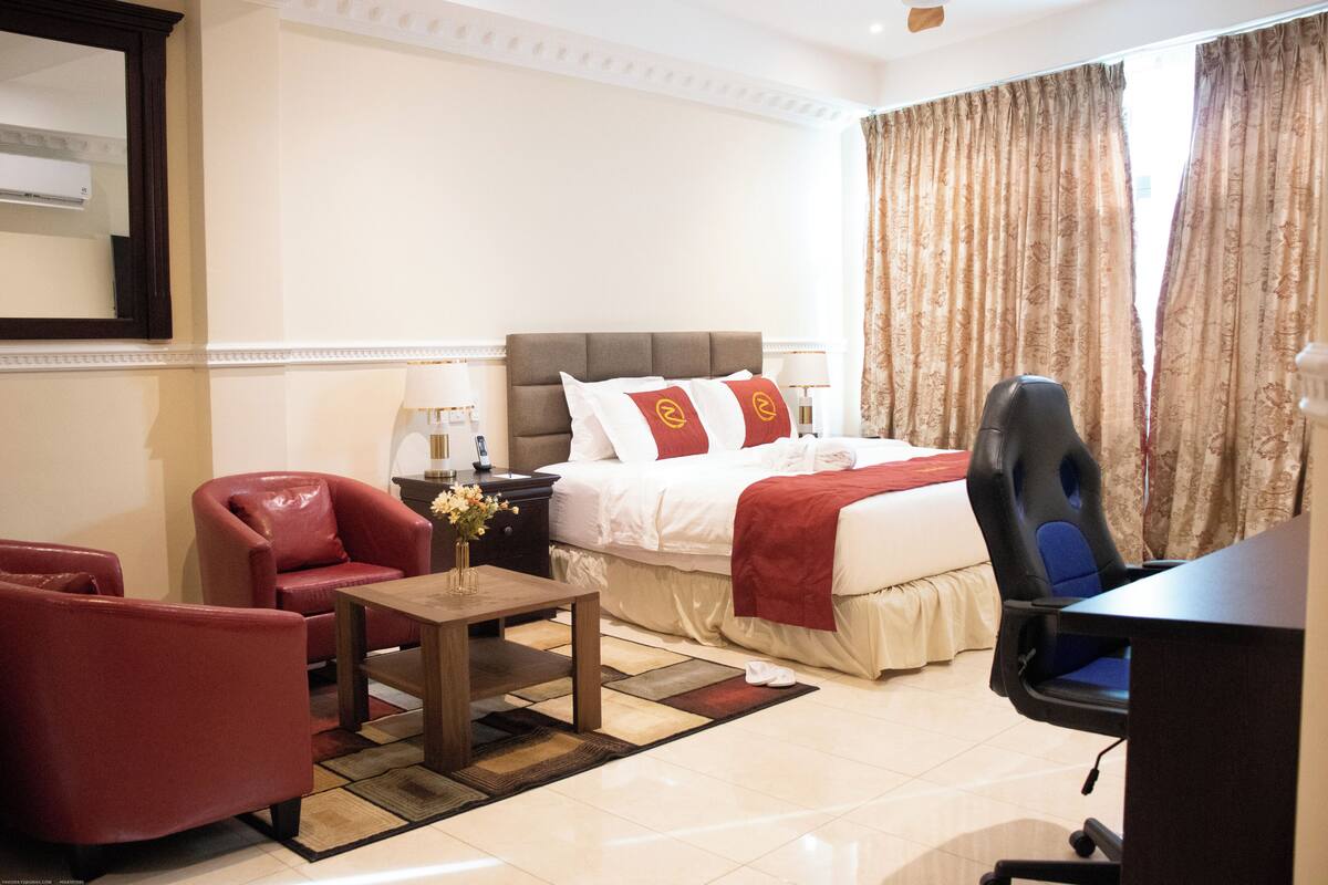 A hotel room with a bed, a desk, a chair, a nightstand, and a mirror.