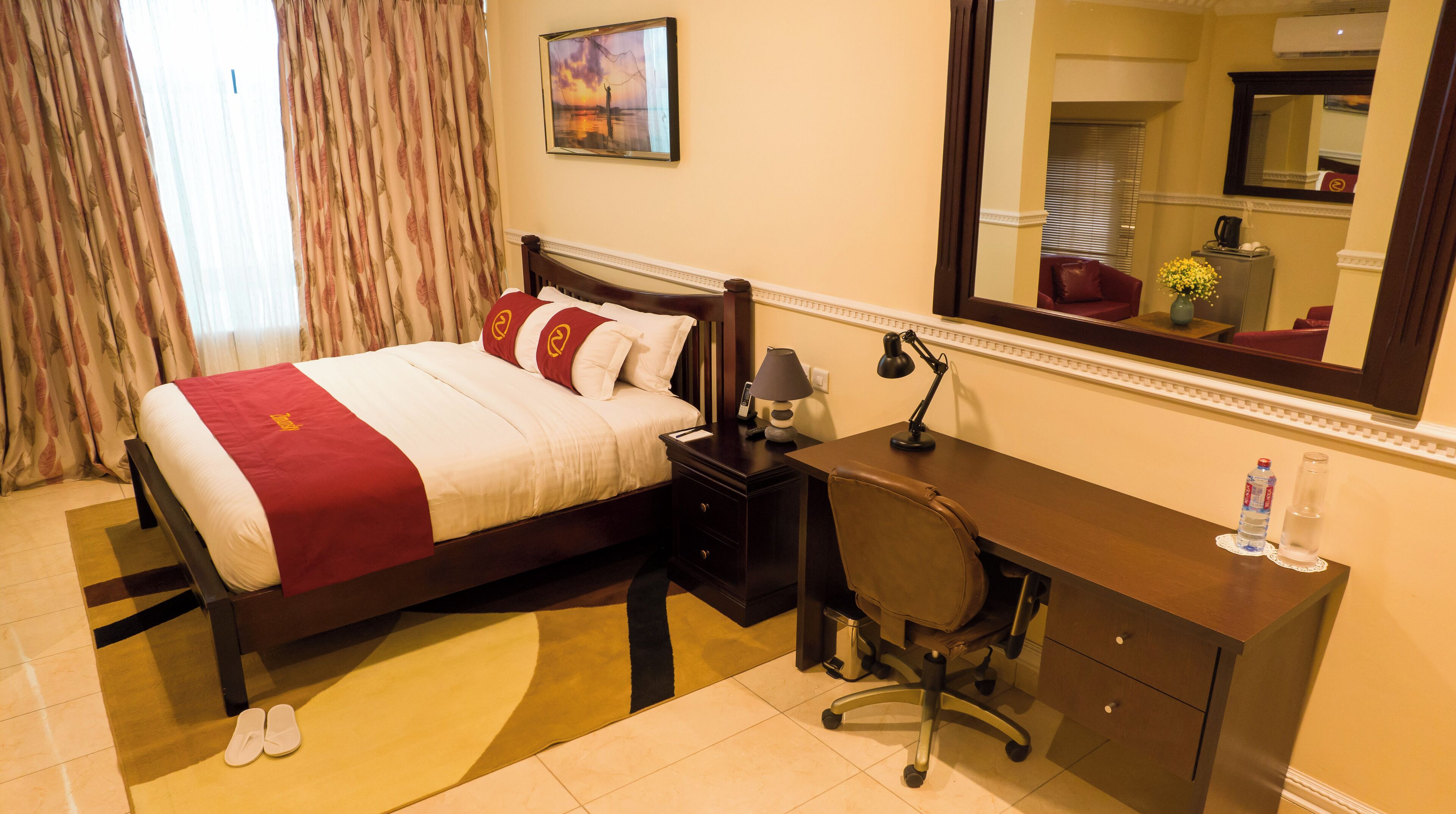 Une chambre d’hôtel avec un lit, un bureau, une chaise et un grand miroir.