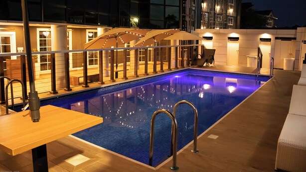 A swimming pool with a wooden deck, lounge chairs, and umbrellas. - Zimansky Hotel  (Accra)