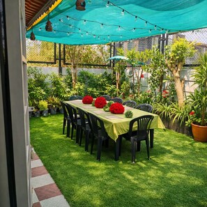 Un espace de restauration en plein air avec une table dressée pour six personnes, entourée de chaises, sous une tonnelle verdoyante.