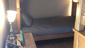 Un lit superposé avec un bureau et une lampe, des murs en bois et une fenêtre.