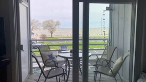 Un balcon avec une table et des chaises, donnant sur une zone herbeuse et un plan d’eau.