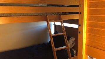 A bunk bed with a wooden ladder, a small shelf, and a wardrobe.