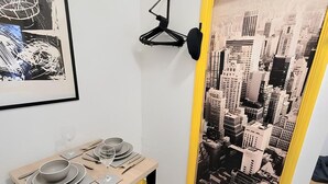 Un coin repas avec une table dressée pour deux personnes, un porte-manteau noir accroché au mur et une fresque représentant un paysage urbain sur la porte.