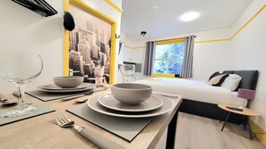 A hotel room with a neatly set dining table, a bed with a black headboard, and a cityscape mural on the wall.