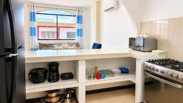 Une cuisine compacte équipée d’un réfrigérateur, d’une cuisinière, d’un four à micro-ondes et de divers ustensiles de cuisine.
