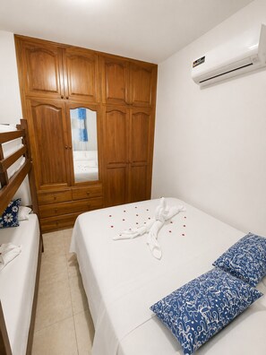 Una camera da letto con un armadio in legno, un letto con piumone bianco e cuscino a motivi blu, e un condizionatore d'aria a parete.