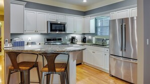 A kitchen with white cabinets, stainless steel appliances, a granite countertop, and two bar stools. - Clayton Resort Getaway w/ Pool Access, Pickleball! (Clayton)