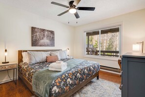 A bedroom with a bed, a ceiling fan, a window with a view, and a nightstand with a lamp. - Maggie Valley Mtn Escape w/ Fire Pit & Deck (Maggie Valley)