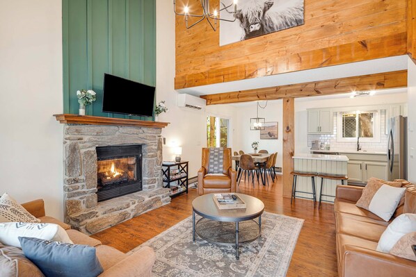 A spacious living room with a stone fireplace, leather sofas, and a dining area with a high ceiling and wooden beams. - Maggie Valley Mtn Escape w/ Fire Pit & Deck (Maggie Valley)