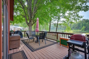 Una terraza de madera con mobiliario exterior, una parrilla y vistas a un lago.