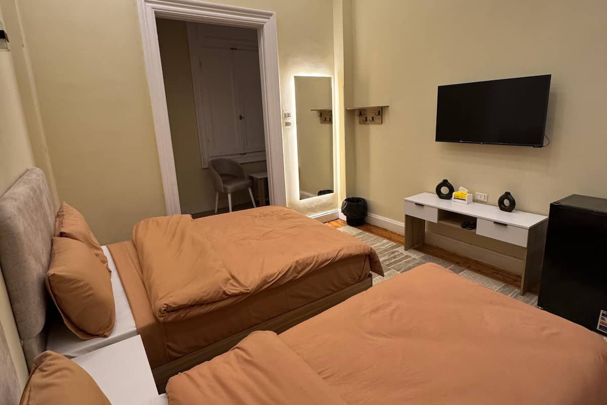 Ein Hotelzimmer mit zwei Betten, einem Fernseher, einem Schreibtisch und einem Spiegel.